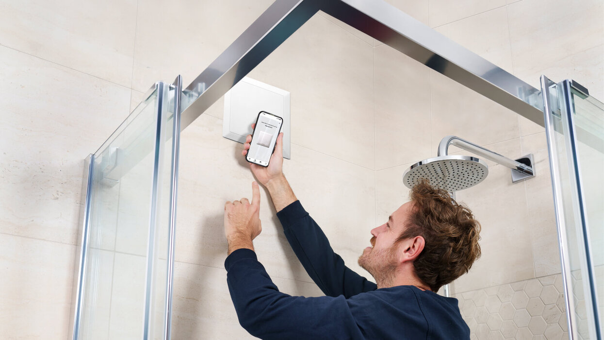 Person kontrolliert die Einrohrlüftung in der Dusche mit einem Smartphone.