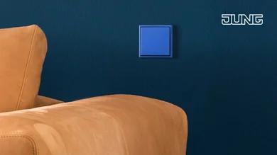 Hellbraunes Sofa vor einer dunkelblauen wand. An der Wand ist ein hellblauer Schalter.
