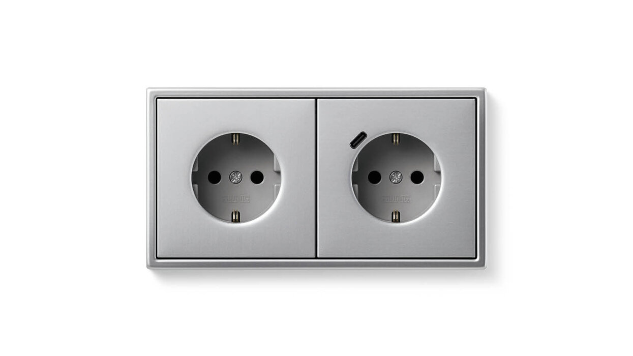 Zwei Steckdosen in der Farbe Silber vor einem hellen Hintergrund. Die rechte Steckdose hat auch einen USB-Anschluss.