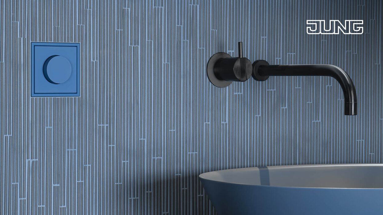 Waschbecken in der Farbe Graublau und einem Wasserhahn, der an der Wand montiert ist. Daneben ein hellblauer Dimmer des Herstellers JUNG.
